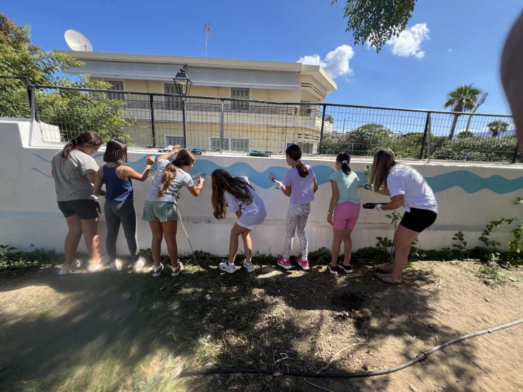 Volunteers paint blue waves on a community wall in Chania.