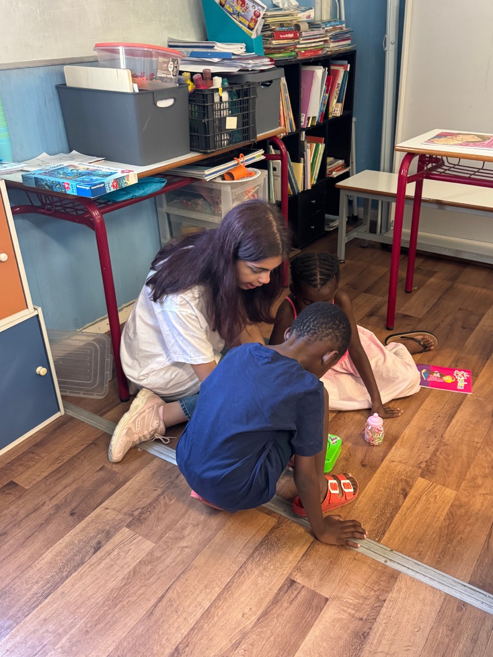 A volunteer sits on the classroom floor with two children during an activity.