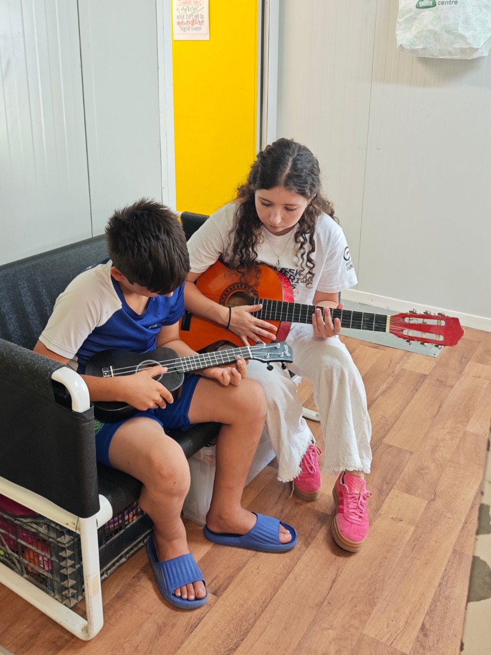 A volunteer and a child play guitar and ukulele together in a classroom.