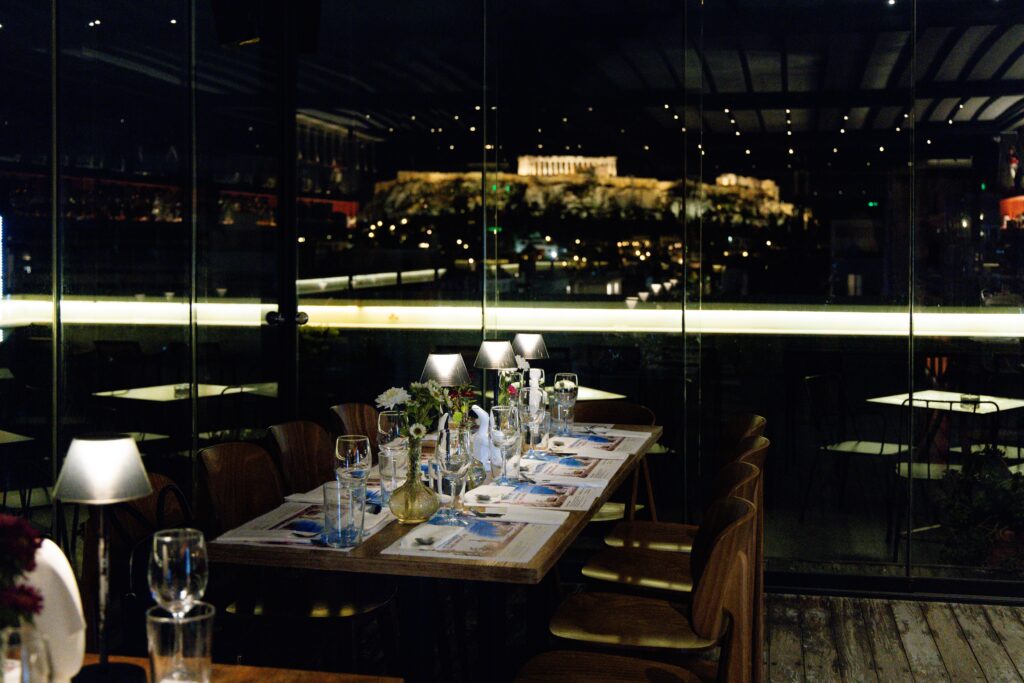 Dinner tables and the illuminated Athens skyline through the rooftop windows.